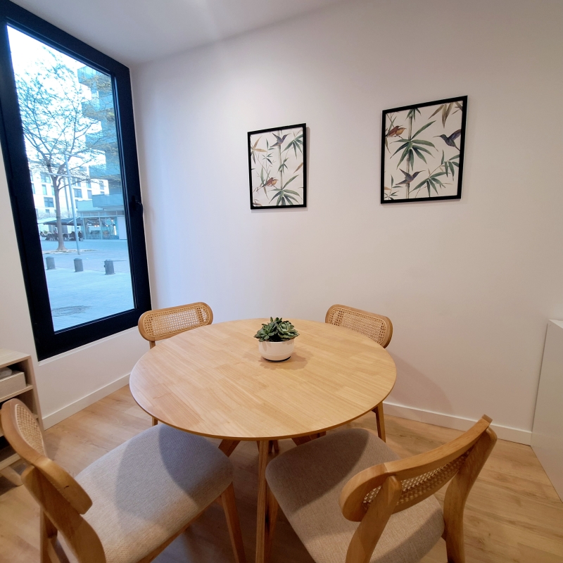 A round table with four chairs around it. Two pictures on the wall. A window.